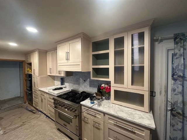 Cream cabinetry with a professional range, marble backsplash and glass-front uppers