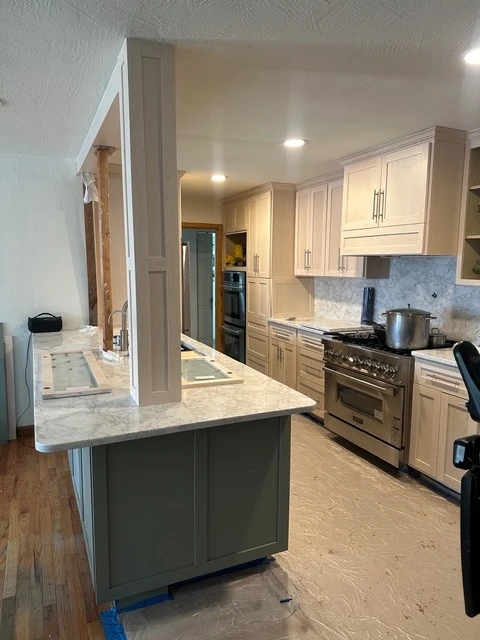Green island with a marble counter beside cream perimeter cabinets