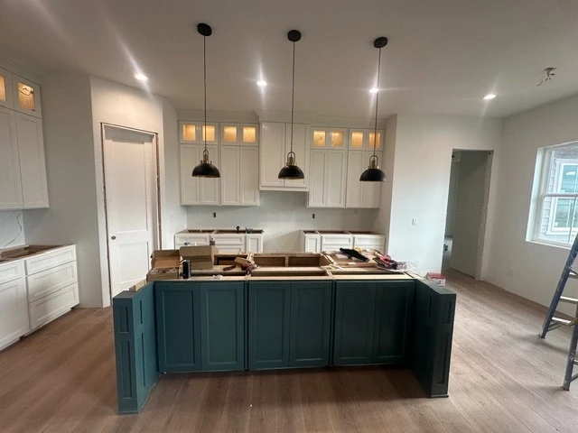 Open-plan kitchen with white upper cabinets and a deep teal island under black pendants