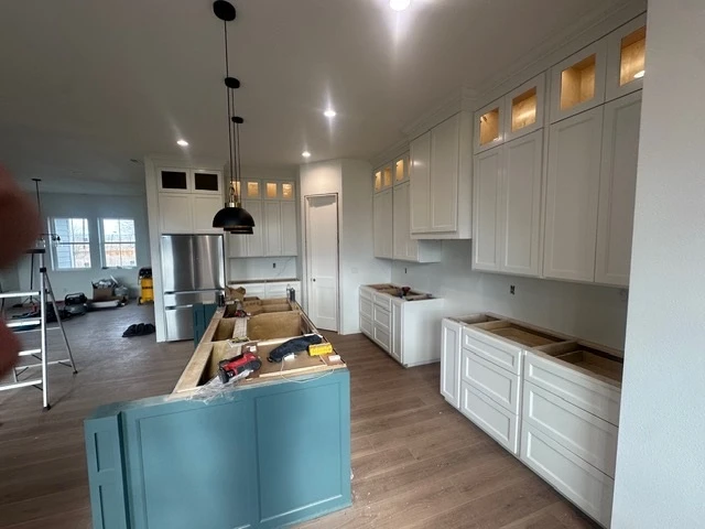 Wide view of an open-plan kitchen with a teal island and white cabinetry