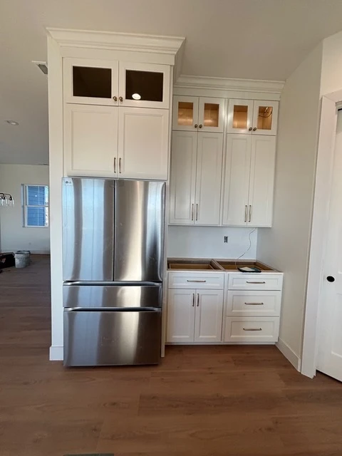 White kitchen with glass-front upper cabinets and a stainless refrigerator